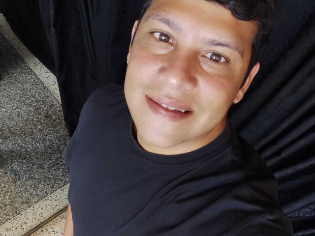 JustinBerry with short black hair, brown eyes, smiling, wearing a black shirt, small ear ring, and a slightly chubby face, taking a selfie.
