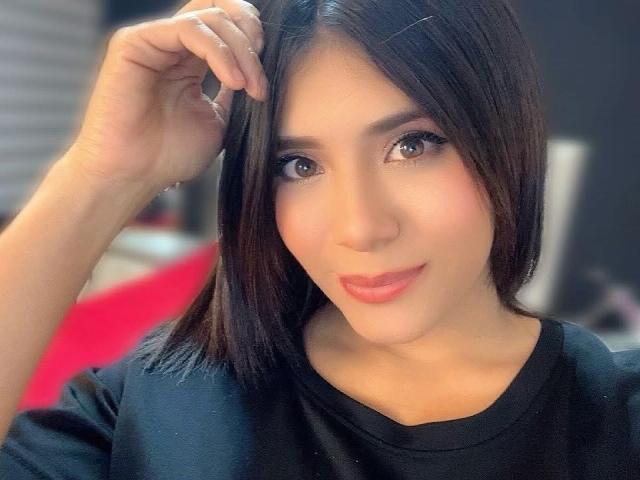 LucieMilner has smooth, fair skin, dark brown eyes, and straight black hair with a side part. She's wearing a black shirt, looking cute with a slight smile.