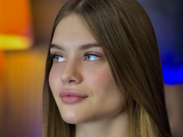 LuisaClover has blue eyes, straight brown hair, and pink lips. Her nose is small and her skin is fair. She's looking to the side with a slight smile.