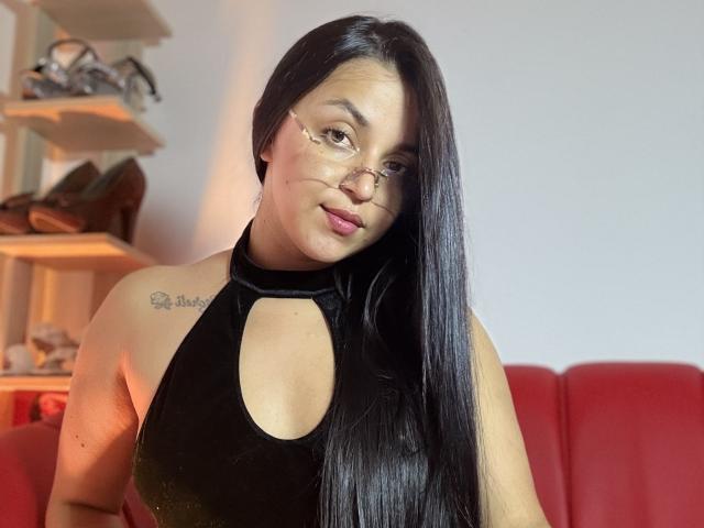 HikariChloe with long black hair, wearing glasses and a black halter top, showing her tits in a photo. She has a tattoo on her right shoulder.