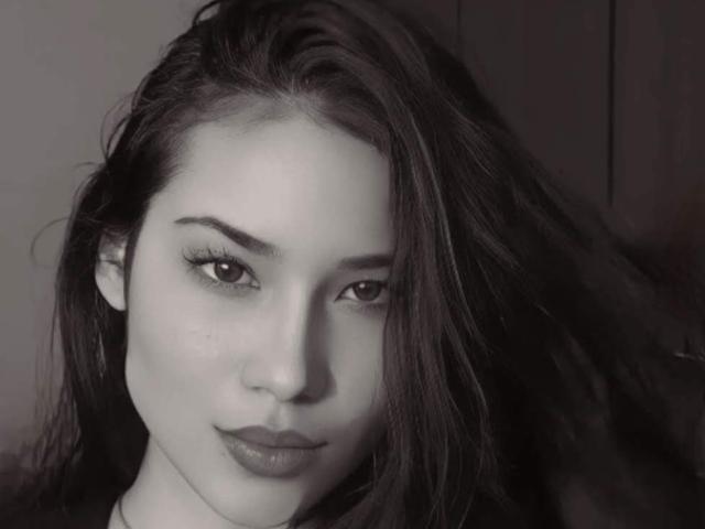 GeorginaFit has dark, wavy hair, light skin, and a subtle smile. Her small, dark eyes and full lips are prominent. She's looking directly at the camera with a calm expression.