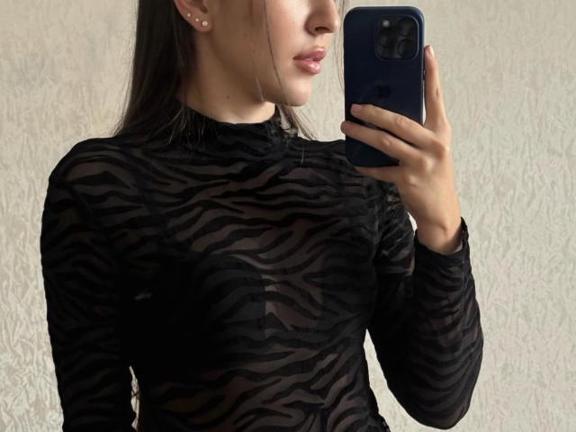 AquaLady with zebra-patterned black sheer top, holding a blue phone in her right hand, taking a mirror selfie, showing her tits and nipples through the transparent fabric.