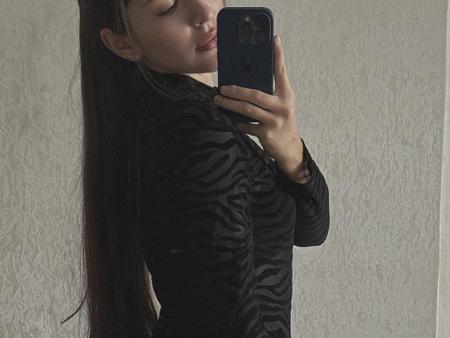 AquaLady with long brown hair, wearing a black zebra-patterned top, taking a mirror selfie with her phone, showing her side boob, and a subtle smile.