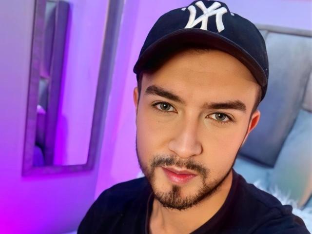 DaltonWhite tiene una cara simpática, lleva una gorra negra de NY, una camiseta negra y una pequeña barba, con una leve sonrisa y una expresión relajada. Está mirando directamente a la cámara..