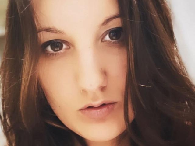 ZafiraMoonn's face with brown eyes, slightly parted lips, and wavy brown hair, looking directly at the camera with a neutral expression. Her nose is small and her skin is fair.