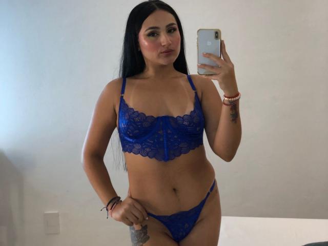 HiilaryDolce with long black hair, wearing blue lace lingerie, holding a phone, showing her tits and pussy, standing in a mirror selfie, looking confident.