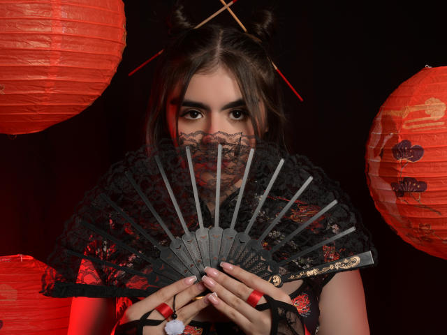 SofiaaFontaine holding a black lace fan, red nail polish, lace mask covering her mouth, red paper lanterns, double bun hairstyle with chopsticks, dark background, Asian-inspired outfit.