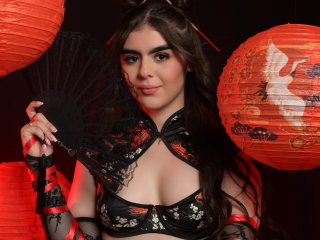SofiaaFontaine with long brown hair, wearing a black lace dress with red floral patterns, holding a black fan, red paper lanterns in the background, cute smile.