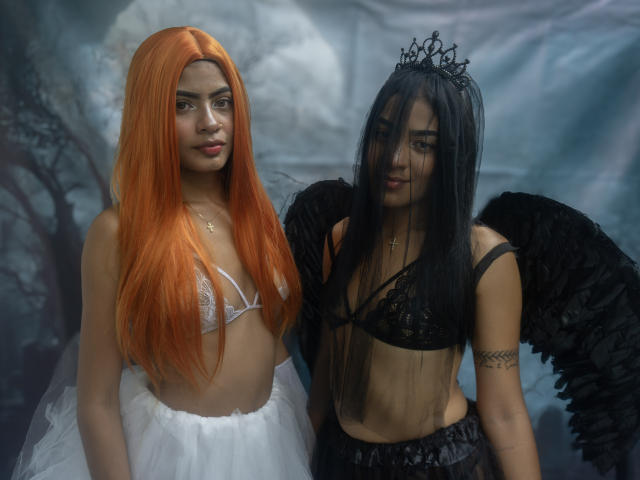 KarenAndLaura, avec des cheveux orange, de petites seins, un soutien-gorge blanc et une jupe, se tient à côté de KarenAndLaura, avec des cheveux noirs, des ailes noires, un soutien-gorge noir et une jupe, et portant une couronne..