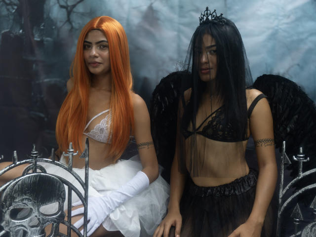 KarenAndLaura with orange hair, white lace bra, and gloves, sitting next to black-haired KarenAndLaura with black wings and black lace bra, both wearing white and black sheer skirts.