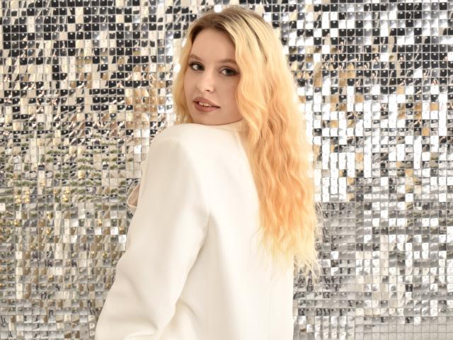 KyleJackson with long blonde wavy hair, white sweater, looking over shoulder, cute face, slight smile, shiny silver mosaic background. She's got a sexy, pretty look, white eyes.