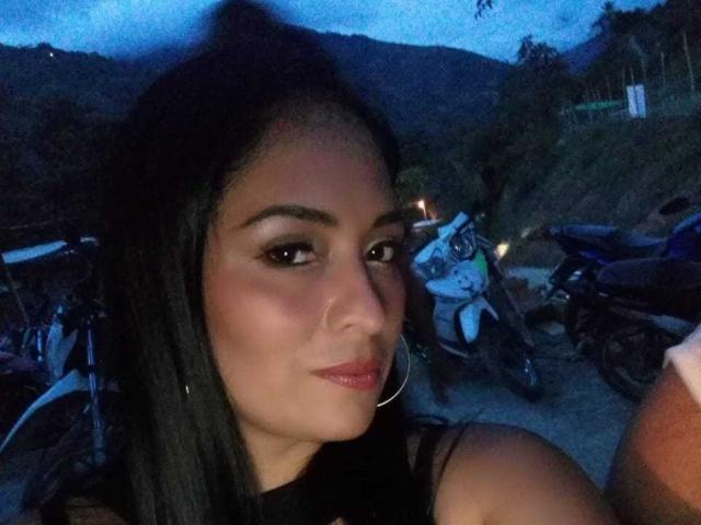 CatleyaSmith with dark hair, hoop earrings, and red lipstick, looking at the camera with a slight smile, in front of parked motorcycles at dusk.