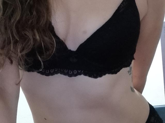 SuaInanna's black lace bra, showing her small tits and slightly visible nipples, with wavy brown hair on the left and a tattoo on her right side.