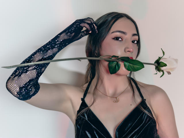 AnnFisher with black lace gloves, holding a white rose in her mouth, wearing a black velvet halter top, her tits slightly visible, brown hair, neutral expression, white background.