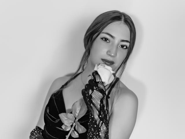 Black-and-white photo of AnnFisher with long hair, holding a rose in front of her face, wearing a lace-patterned sleeve, looking seductively at the camera with her tits visible.