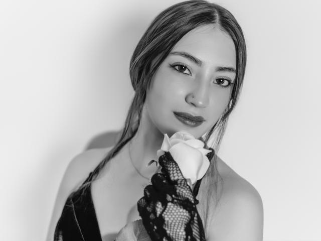 AnnFisher with long hair, holding a rose in a black lace glove, wearing a sleeveless dress, looking at the camera with a slight smile in a black-and-white photo.
