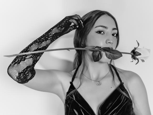AnnFisher with a rose in her mouth, holding a lacy glove to her head, wearing a black velvet top, and a necklace, in a black-and-white photo.