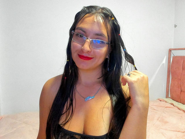 VenusSweetPalmer with long black hair, glasses, red lipstick, and a silver necklace, holding a hair strand, smiling, showing her tits in a black lace top.