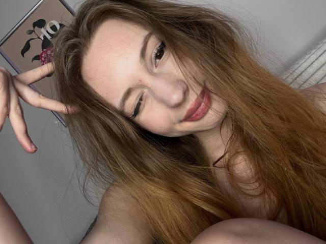 ElfinVibes has long, dirty blonde hair, winks with one eye, and makes a peace sign with her right hand, showing off her small, pink, pouty lips.
