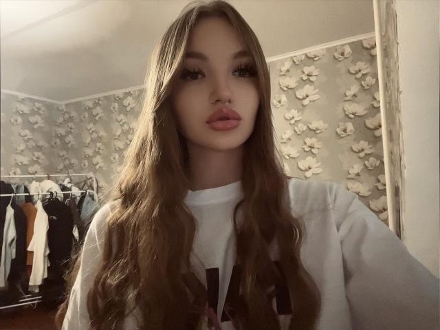 KlarnetHot has long brown hair, full pink lips, and is wearing a white shirt. She has a nose ring and a cute face. Her tits are not visible.