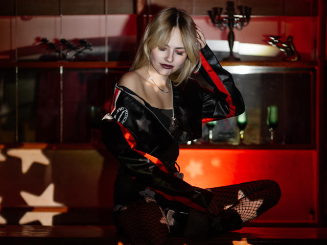 MiaCuteAngel with blonde hair, black star-patterned jacket, red stripes, fishnet stockings, sitting on bar counter, hand in hair, dark lipstick, looking down, red and black lighting.
