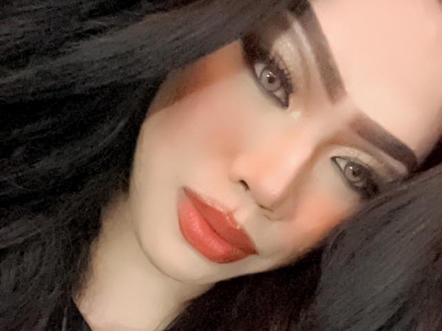 MissCuteBebe has pale skin, red lipstick, black eyeliner, and dark eyebrows with thick black hair, gazing seductively with half-closed eyes. Her ass is not visible.