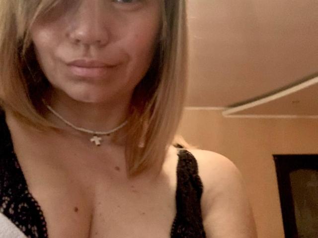 ElizavetaCream has light brown hair, a nose ring, and is wearing a black lace top that shows her big tits. She's smiling slightly with a necklace.