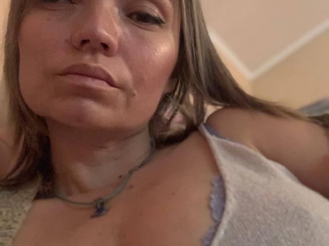 ElizavetaCream with puffy lips, wearing a grey tank top, necklace with a blue pendant, brown hair, slightly sweaty face, looking up at the camera. Boobs visible, medium size.
