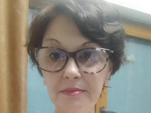 SweetMargoh with short black hair, wearing tortoiseshell glasses, and red lipstick, showing a neutral expression, her nose and eyes clearly visible, with a wooden frame on the left.