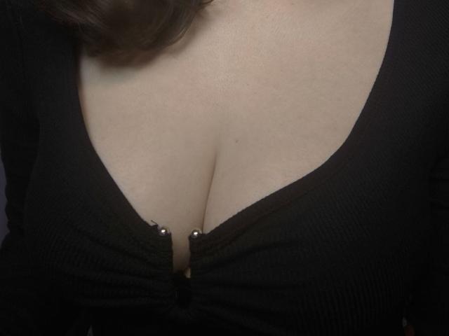 Dreia's big tits in a black, ribbed, low-cut top with a zipper partially open, showing a small bit of cleavage and two metallic zipper pulls.
