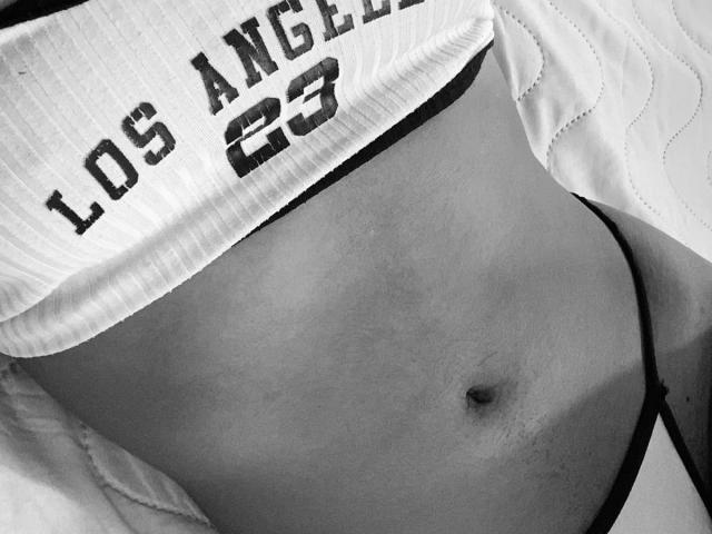 HottieLoveTime's flat, tan-lined belly with a visible navel, wearing a ribbed sports shirt and black thong, showing a partial view of their ass. Black and white image.