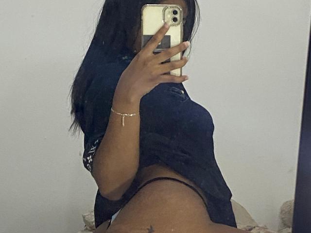 HottieLoveTime with dark hair, black shirt, and black thong, taking a mirror selfie, showing her ass, with her phone covering her face.