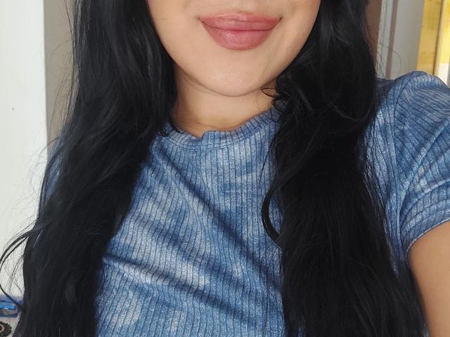 LauraRichis has black, wavy hair, full pink lips, and is wearing a blue, ribbed, short-sleeve shirt. Her skin is light. Her tits are not visible.