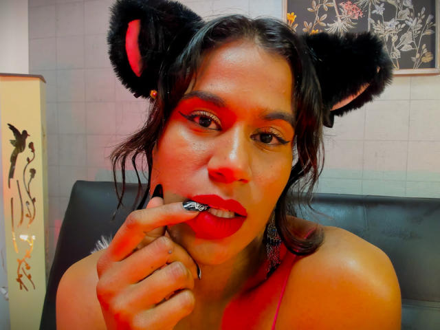 GodessMar with black furry cat ears, red makeup, and glossy red lips, biting her finger, showing off black nail polish, and wet dark hair, looking sexy.