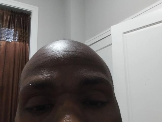 Shauncampbell-hot's bald head is in the foreground, with dark brown skin and slightly parted eyebrows. Door and curtain in background.