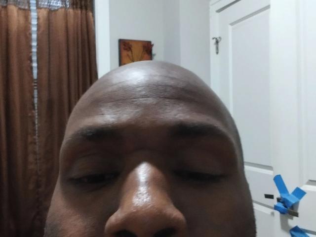 Shauncampbell-hot's bald head, dark brown skin, and slightly closed eyes, with visible eyebrows and nose, in a tight shot, showing a shiny, smooth forehead.