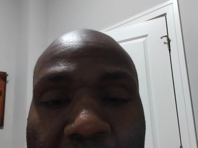 Shauncampbell-hot's dark-skinned face, bald with a small mustache and goatee, showing a slightly serious or tired expression, with a white door in the background.
