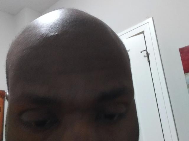 Shauncampbell-hot's bald head and dark eyebrows are centered in the image, with a white door in the background. His eyes are partially visible, looking downward.
