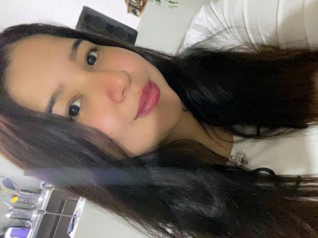 SharaSchart with long dark brown hair, light brown skin, pink glossy lips, and a slight smile, wearing a white shirt, showing her cute face and small nose.