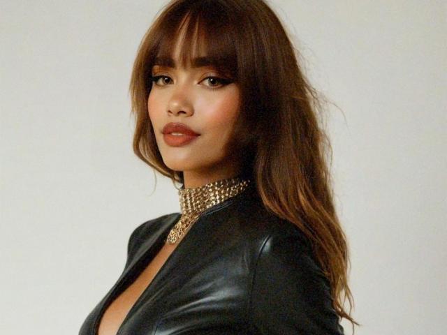 IsabelaLoben with long brown hair, wearing a black leather jacket and gold chain necklace, looking at the camera with a slight smile. Boobs visible through jacket.