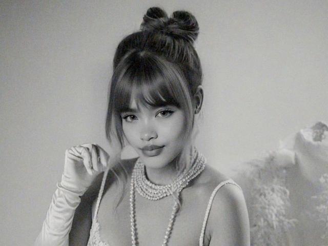 Black-and-white photo of IsabelaLoben with her hair in a bun, wearing a pearl necklace and long gloves, holding a cigarette, showing off her tits and a cute face.
