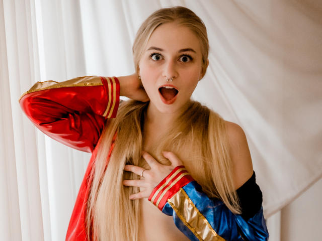 MiaMeowa with blonde pigtails, wearing a red, blue, and gold shiny jacket, hand on chest, mouth open, looking surprised, nipples visible, light skin, cute, sexy.