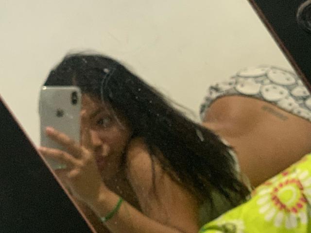 DreamingOfU with long dark hair, lying on bed, taking mirror selfie with iPhone, showing her butt in patterned underwear, green bracelet on wrist, slightly blurry mirror reflection.