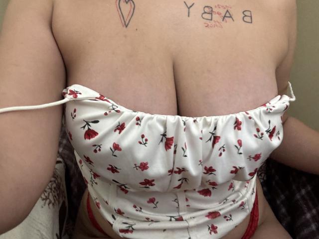 Kametia's big, round tits are covered by a white, floral, strapless top. Red flower pattern. Her tattooed chest is visible. She's wearing red lace underwear.