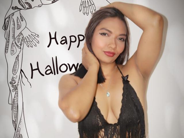 ValeriaJazz with medium tits in a black lace halter top, hands in her short brown hair, wearing a silver necklace, smiling softly at the camera.