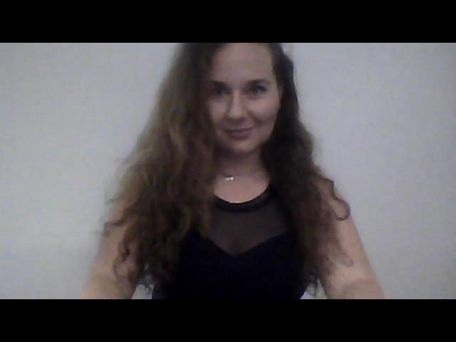 AgnesPretty with long, wavy brown hair, smiling, wearing a black, sheer-shoulder top, has a small, cute ass, and a subtle, confident look in a blurry selfie.