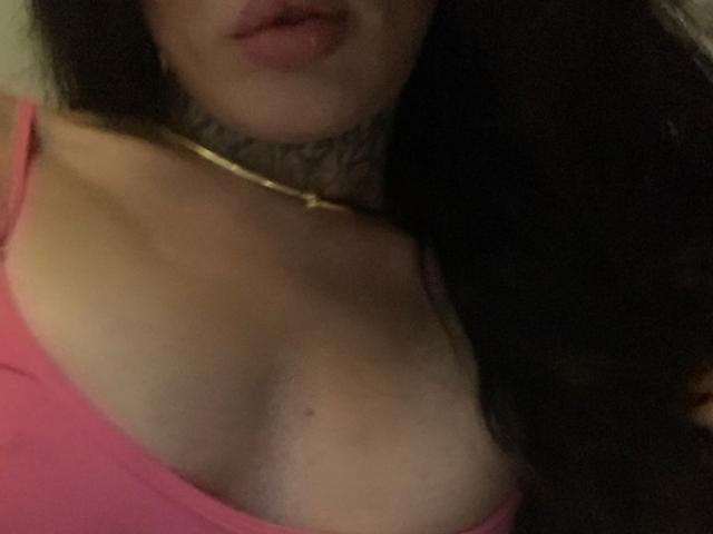 Becab's chest with visible cleavage in a pink top, wearing a gold necklace and a choker, with long dark hair and slightly parted pink lips.