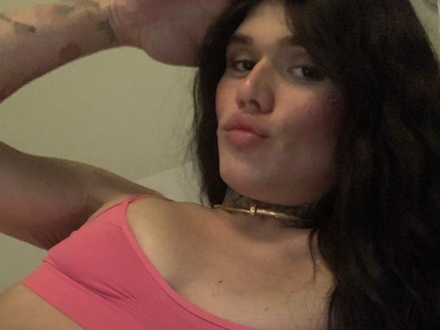 Becab with puffy pink tits, wearing a gold choker, has black hair, tattoos on her arm, and a smug expression, with her hand on her head.