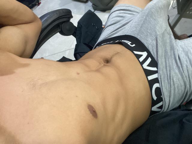 Os abdominais tonificados e musculosos de SteveWolf, com um pequeno mamilo marrom escuro e um umbigo visível, vestindo cuecas cinzas da marca Calvin, deitado em uma cadeira preta..