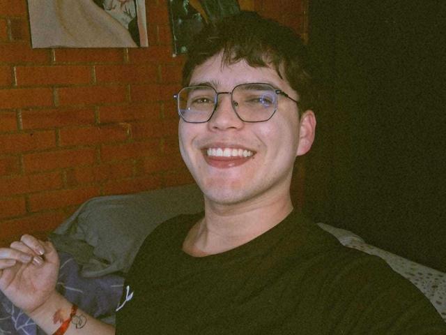 EddTerence is a smiling dude with glasses, short brown hair, and a black t-shirt, showing a ring on his right hand. His ass is not visible.